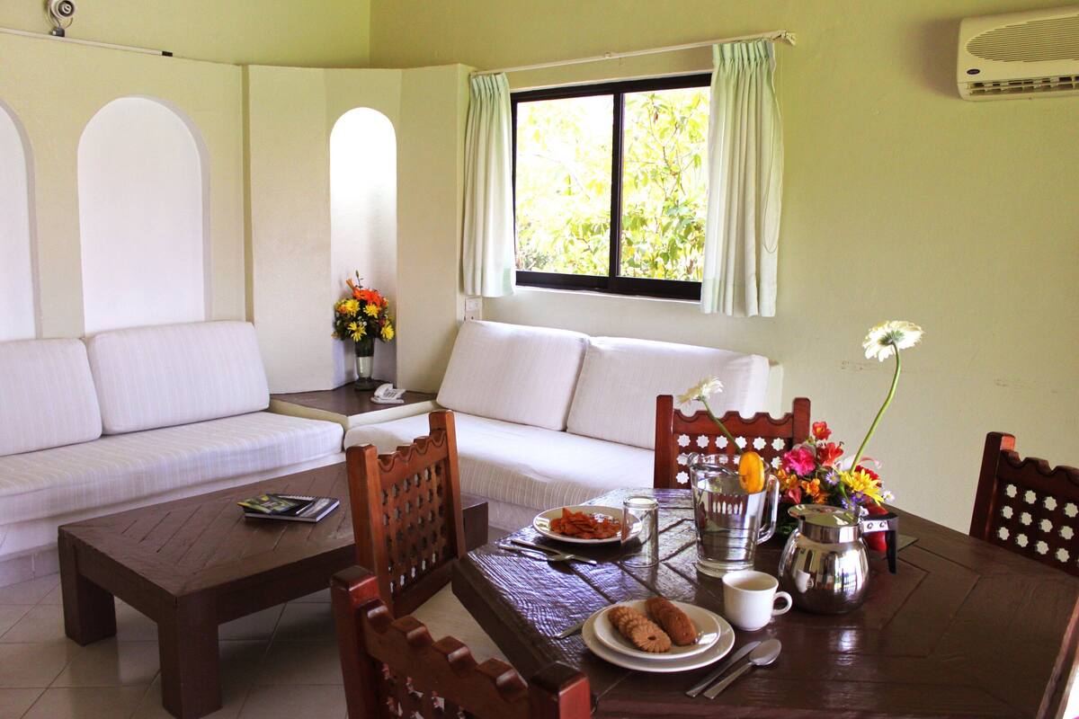 A dining area with a wooden table, chairs, a sofa, and a window with curtains.