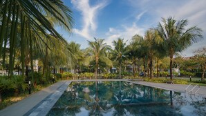A swimming pool surrounded by palm trees and greenery, with a clear sky above. - Kosmos Apart Hotel (Phu Quoc)