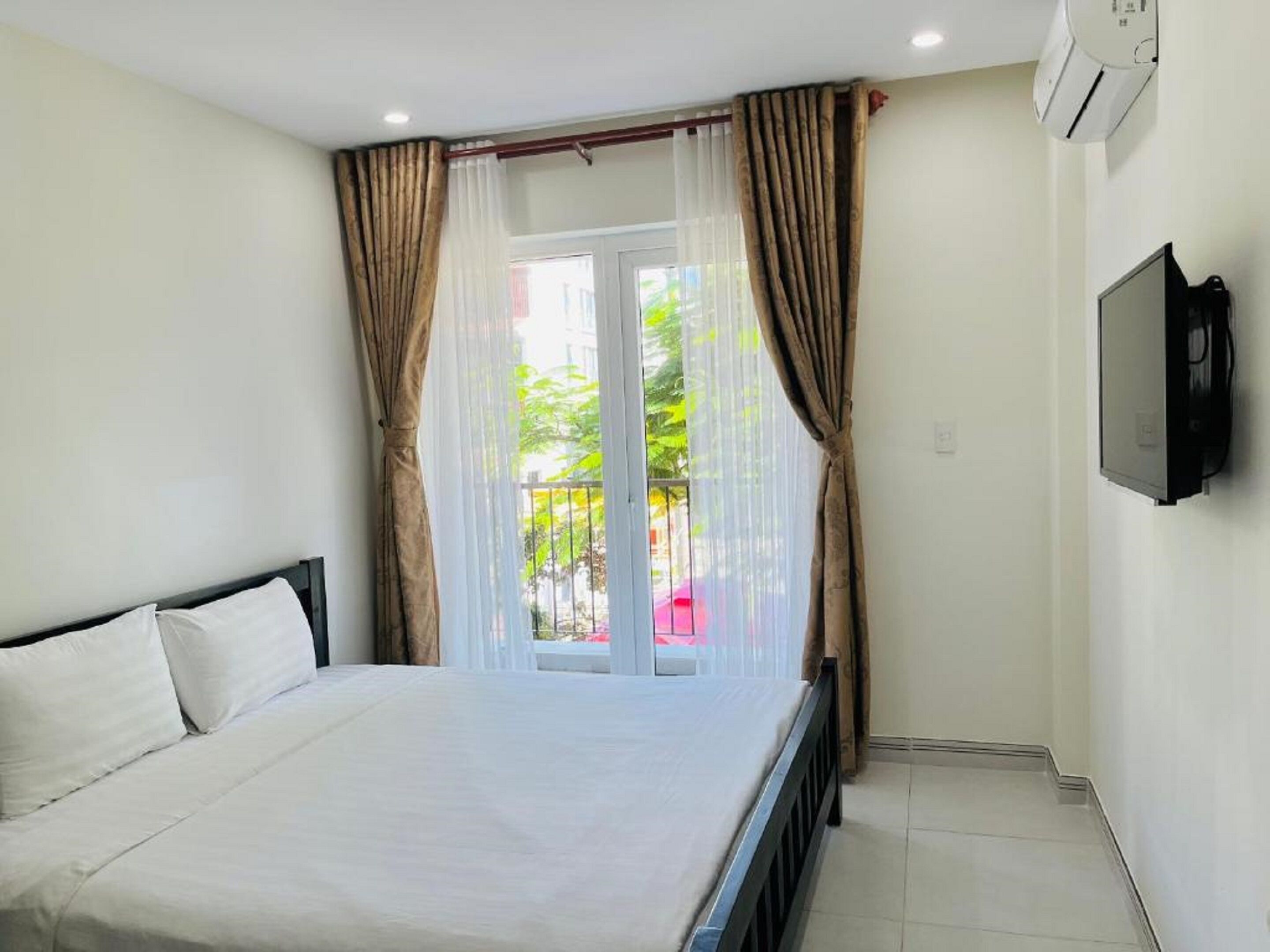 Een hotelkamer met een bed, gordijnen, een televisie en een balkon met uitzicht op groen.