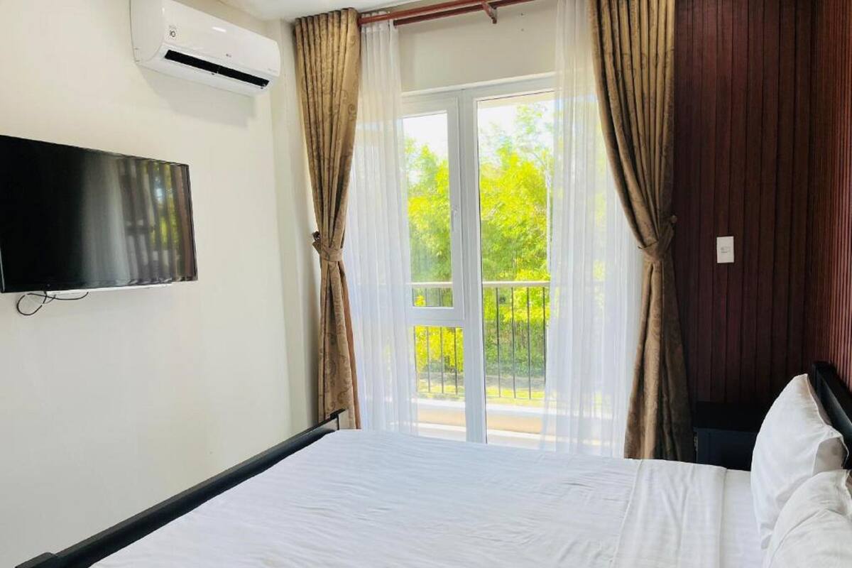 A hotel room with a bed, a TV mounted on the wall, and a balcony with curtains.