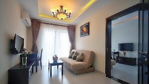 A modern living room with a sofa, a coffee table, a TV, and a chandelier. - Kosmos Apart Hotel (Phu Quoc)
