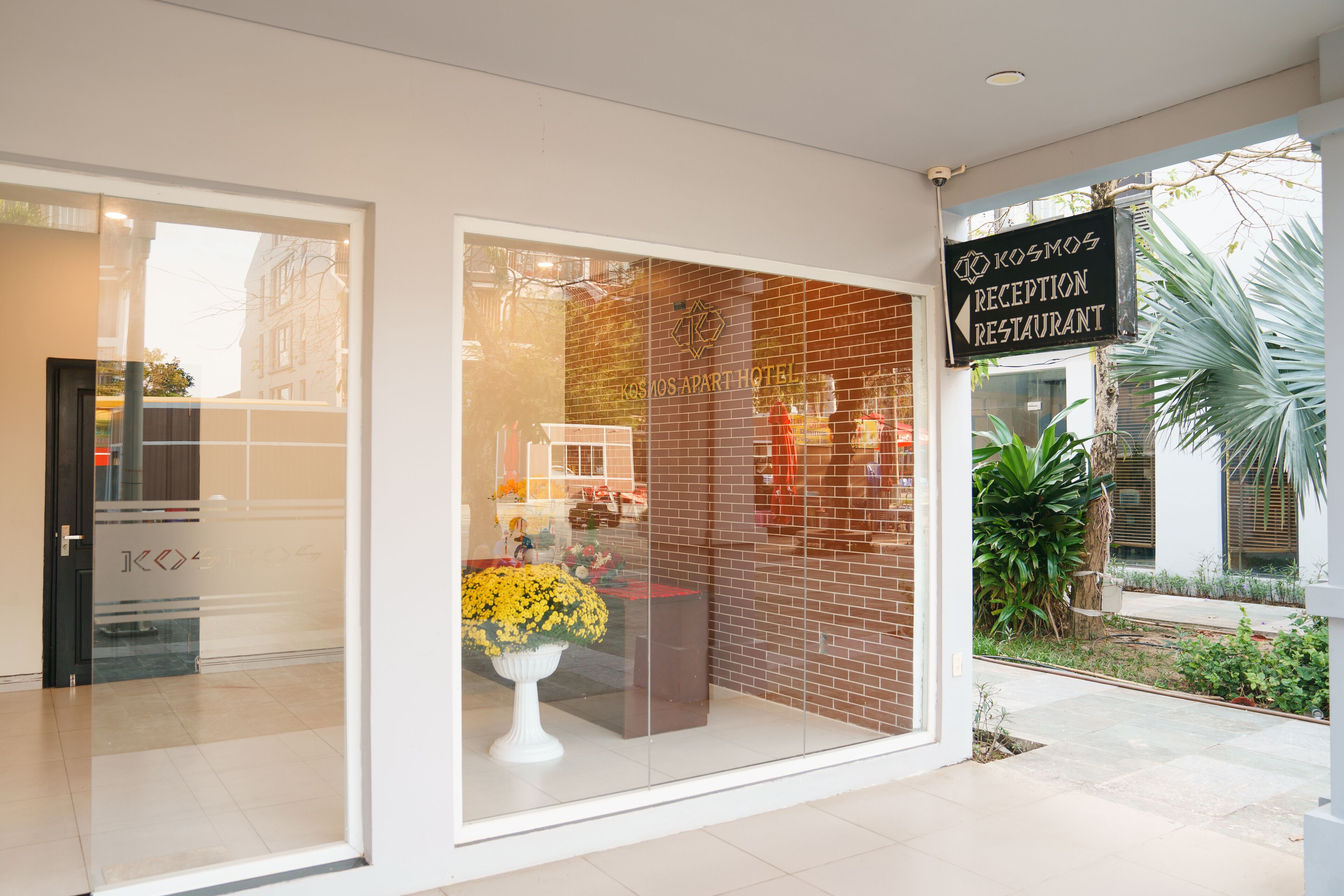 A hotel reception area with a glass door, a potted plant, and a sign for the reception restaurant.