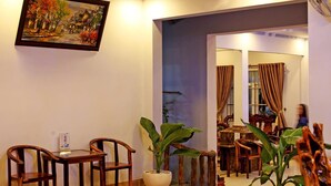 A room with a dining area featuring wooden chairs and a table, a large potted plant, and a painting on the wall. - Thanh Trung Hotel (Phu Quoc)