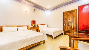 A hotel room with two single beds, a wooden nightstand with a vase of flowers, a wooden door, and a glass table. - Thanh Trung Hotel (Phu Quoc)