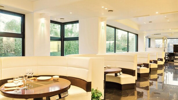 A modern hotel lobby with a long row of white cushioned seating, a polished marble floor, and large windows offering a view of greenery outside. - Setouchiso (Sakaide)