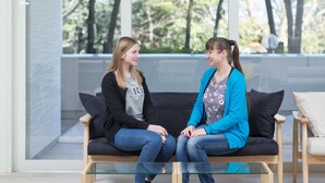 Two people sitting on a black couch with a glass coffee table in a room with large windows and a view of trees. - Setouchiso (Sakaide)