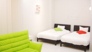 A hotel room with two beds, a green chair, and a white wall with a small picture. - Setouchiso (Sakaide)