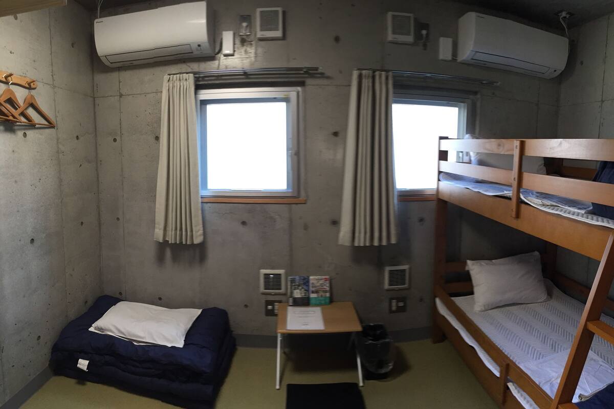 A compact room with bunk beds, a small table, and two windows with curtains.