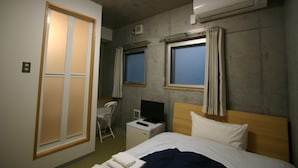 Una habitación de hotel con una cama, un escritorio, una silla y dos ventanas.