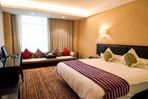 Habitación de hotel con una cama grande, sofá cama, escritorio y ventana con cortinas.