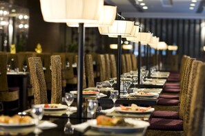 Un restaurante con filas de mesas, cada una con una lámpara, sillas y platos de comida.