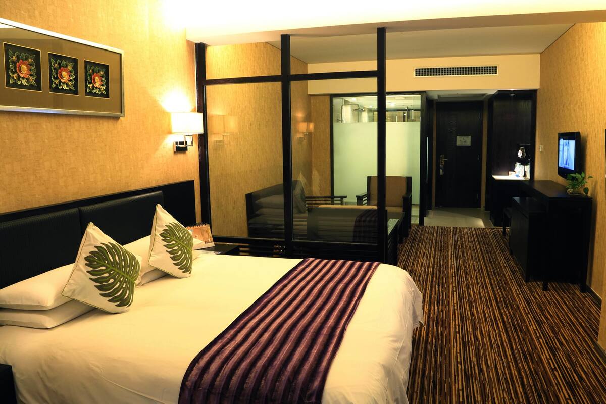 Una habitación de hotel con cama, un espejo grande, un televisor y un escritorio con computadora.