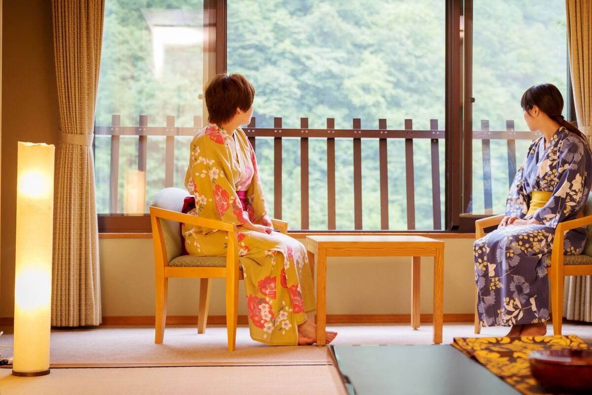 Una habitación japonesa tradicional con suelo de tatami, una mesa de madera baja y dos personas vestidas con kimonos.