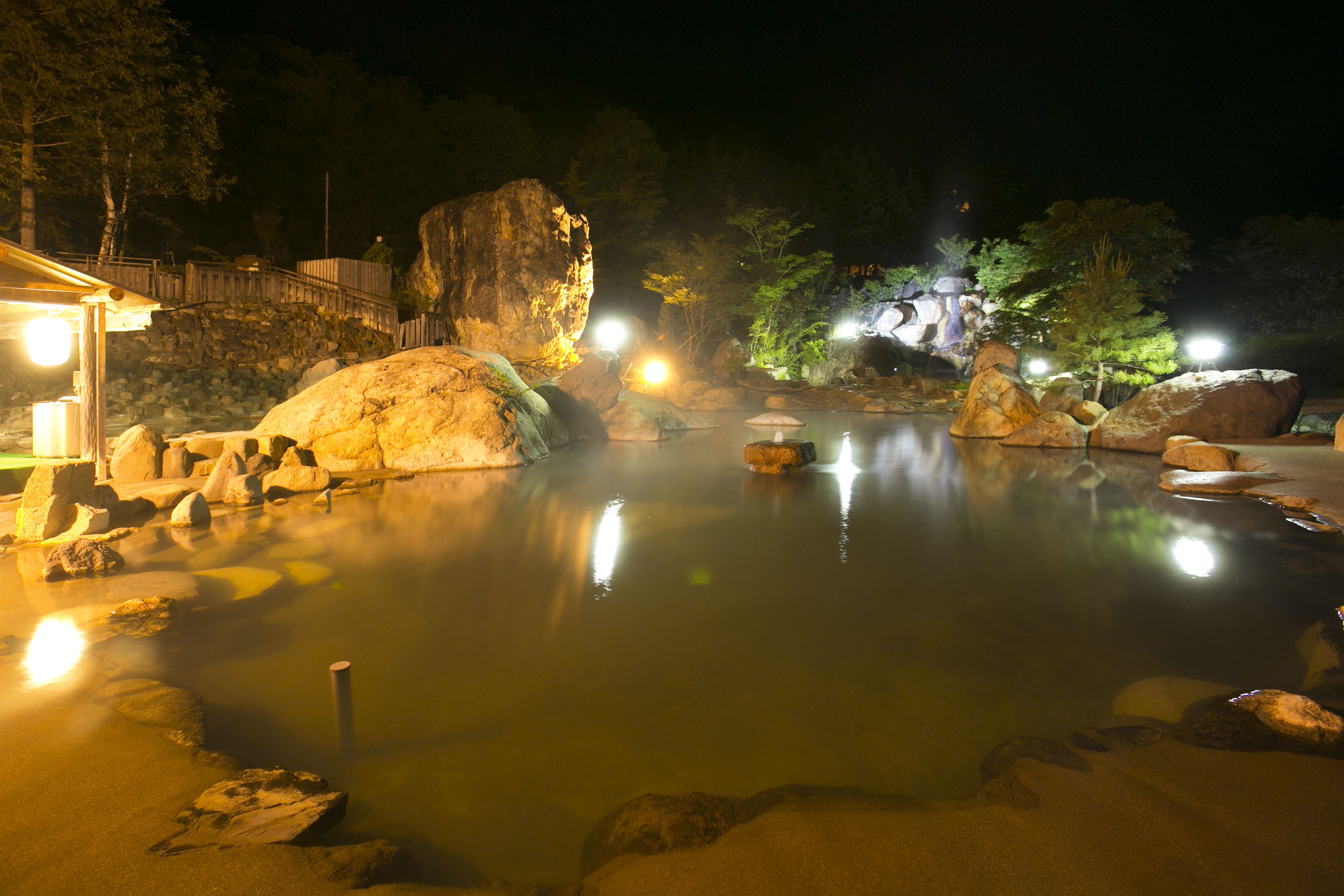 A tranquil outdoor hot spring area with large rocks and a wooden walkway.