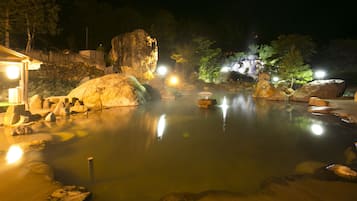 A tranquil outdoor hot spring area with large rocks and a wooden walkway.