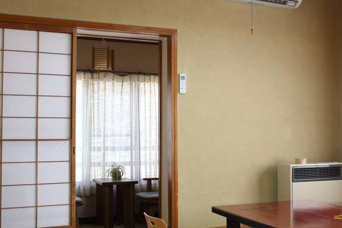 Een kamer met een traditionele Japanse shoji-schuifdeur, een klein tafeltje met een stoel, een luchtverwarmer aan het plafond en een raam met uitzicht.