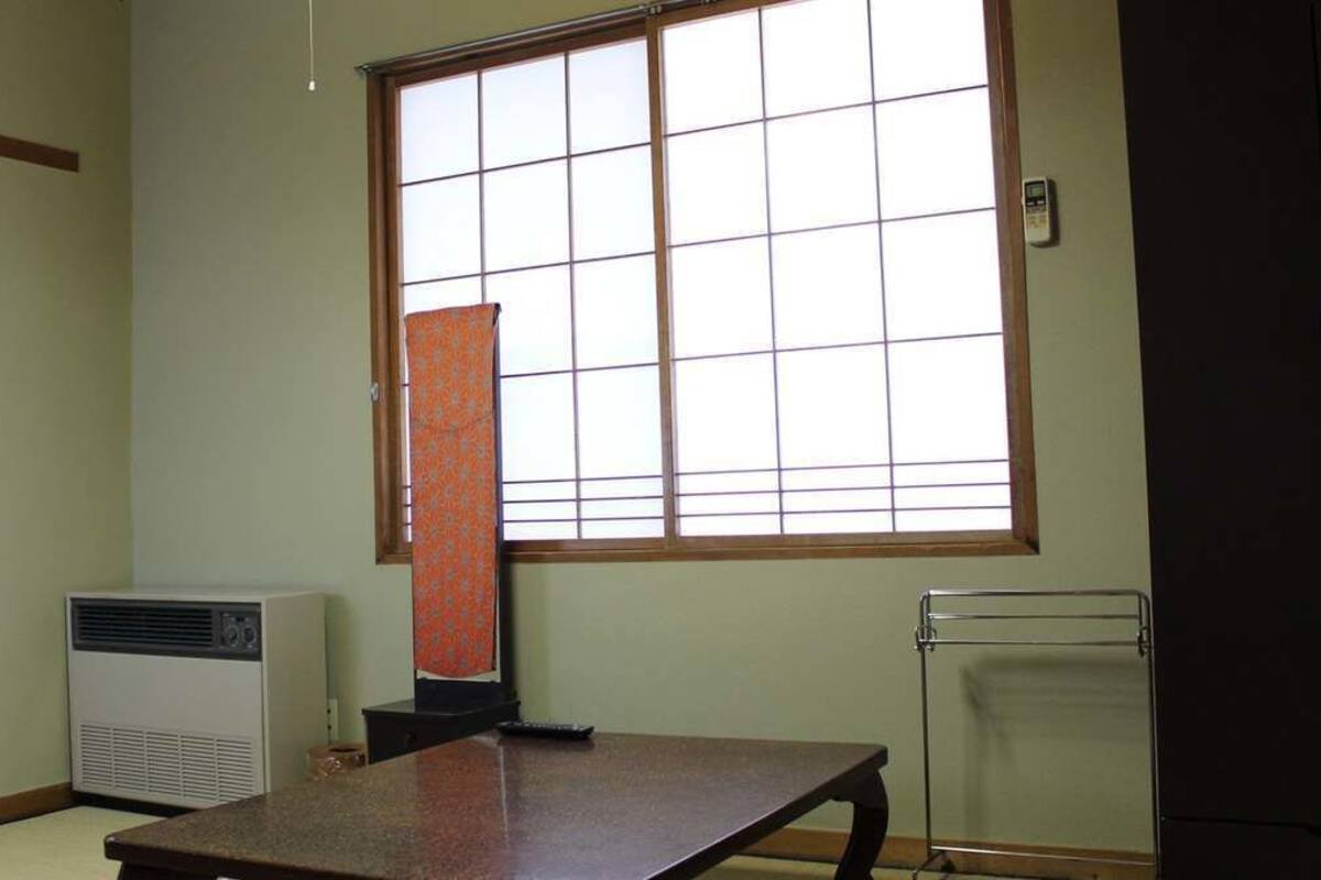 Een kamer met een groot raam, een elektrische kachel, een tafel en een radiator.