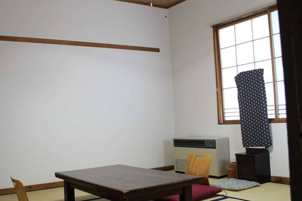 Een traditionele Japanse kamer met tatami vloeren, een lage houten tafel, een donkere kast, een kleine verwarming en een raam met een patroon gordijn.