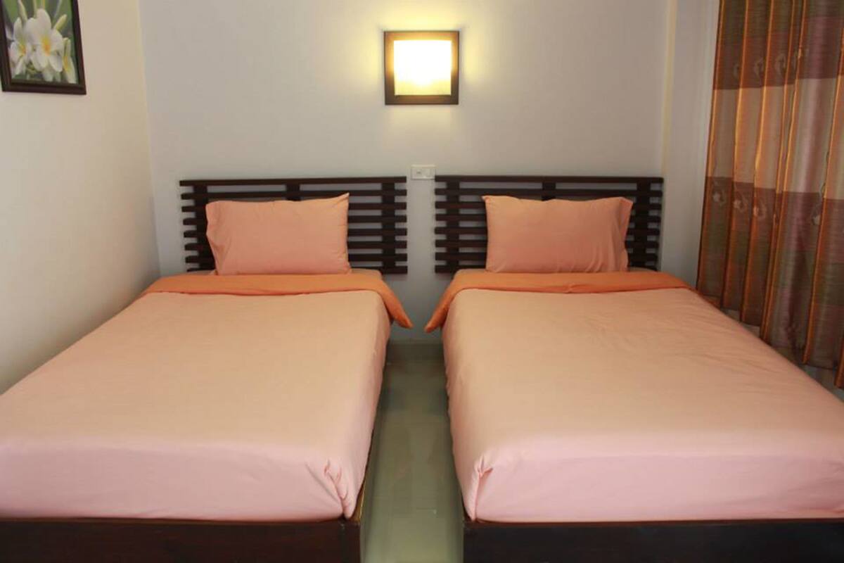 A double room with two beds, each with a wooden headboard and orange bedding.