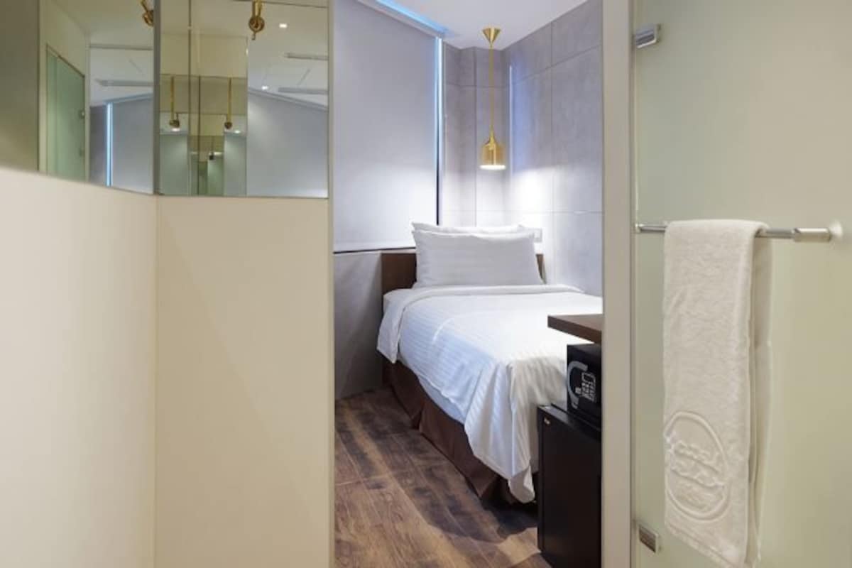 Una habitación de hotel moderna con una cama, una mesita de noche, una toalla y un espejo.