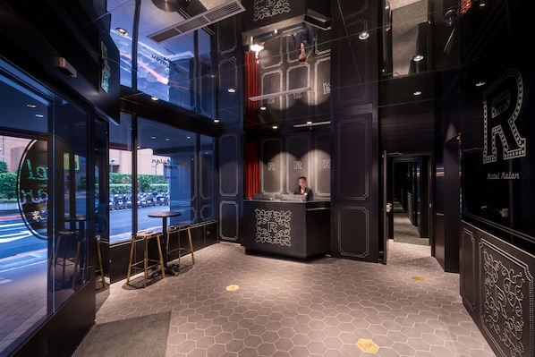 A hotel reception area with a modern design, featuring a reception desk, a large window with a view of the street, and a geometric patterned floor. - Hotel Relax V (Taipei)