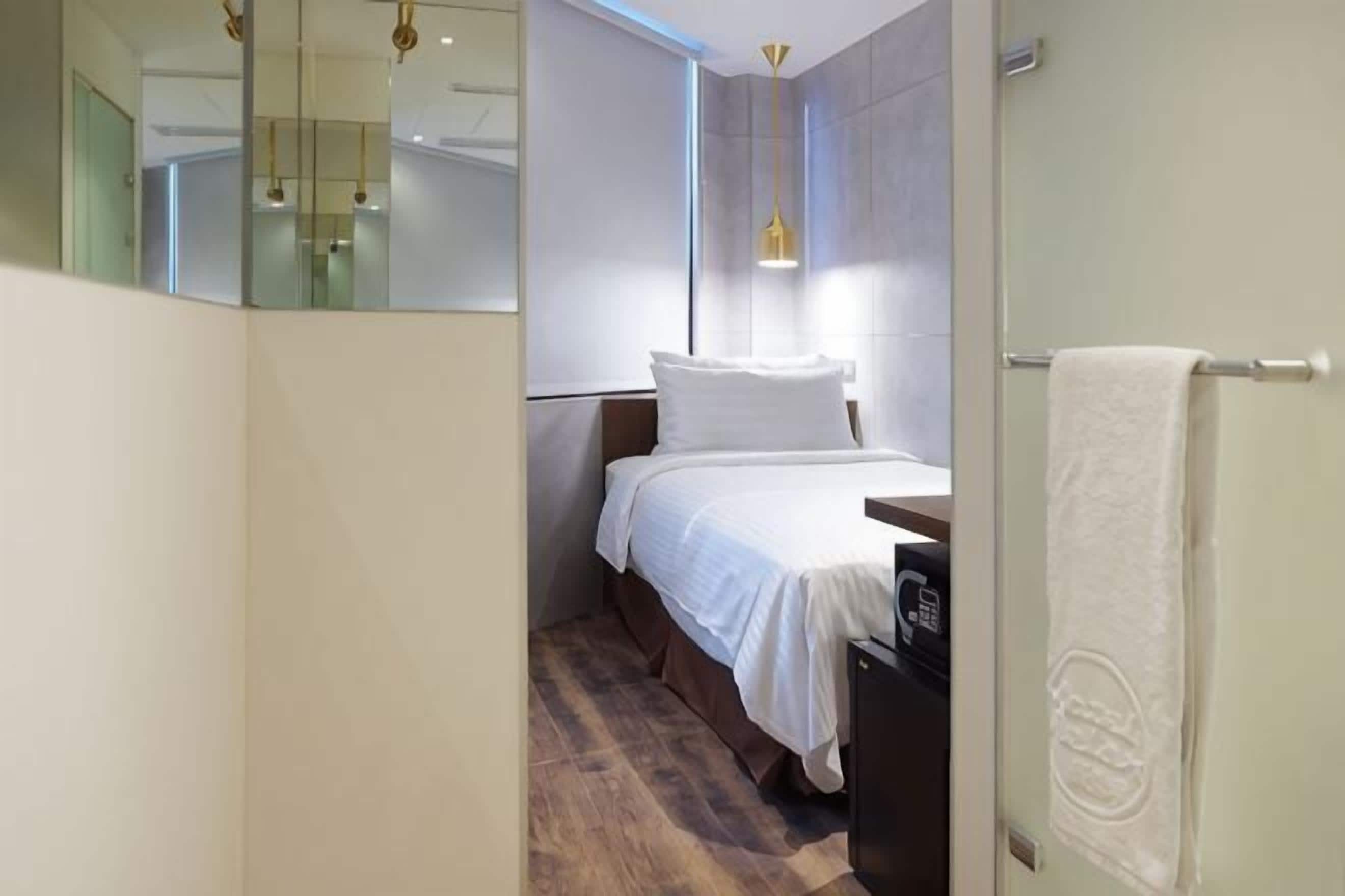Ein modernes Hotelzimmer mit Bett, Nachttisch, Handtuch und Spiegel.