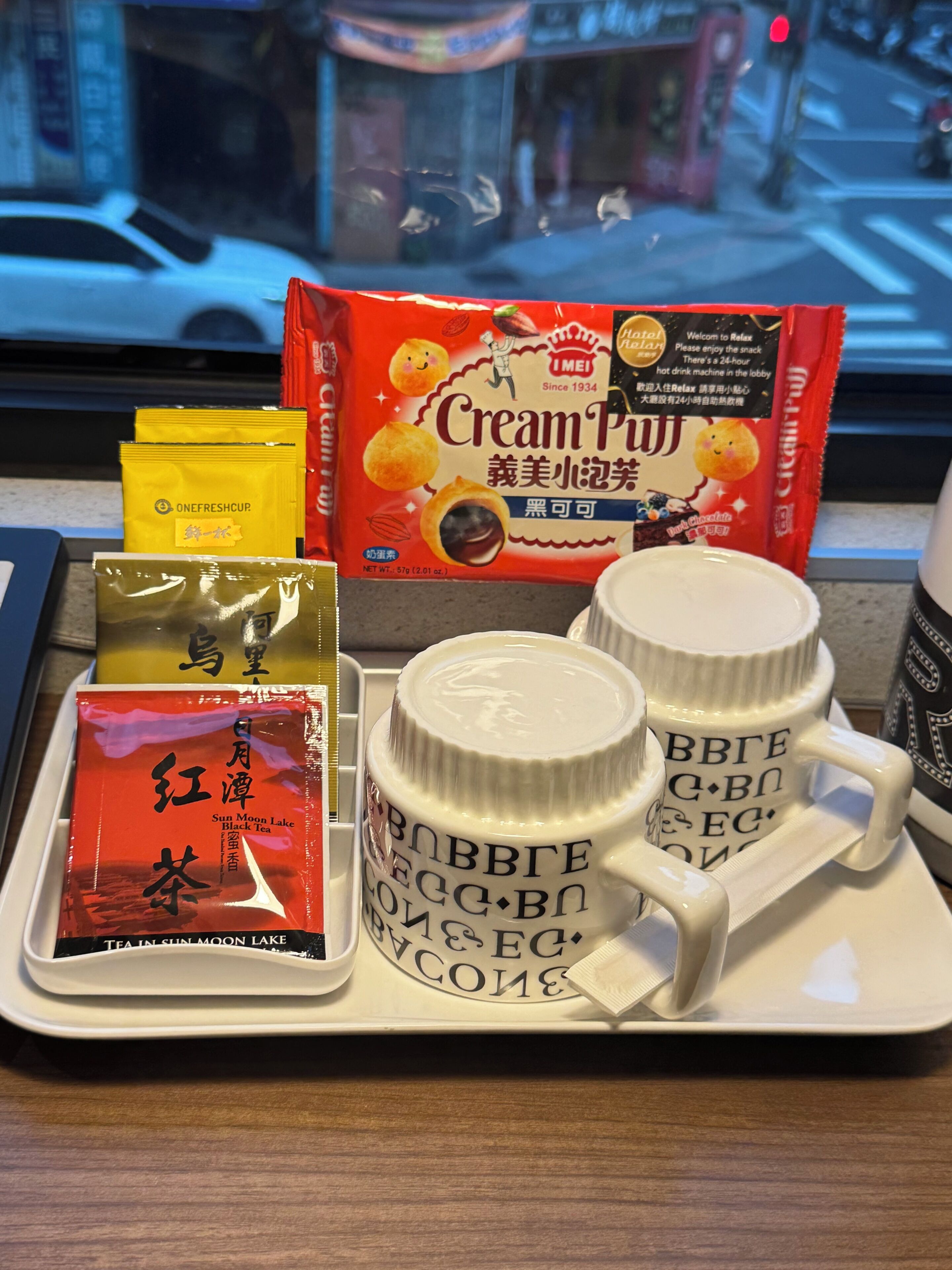 A tray with a pack of Cream Puff, a packet of black tea, and two white mugs with Cyrillic text.