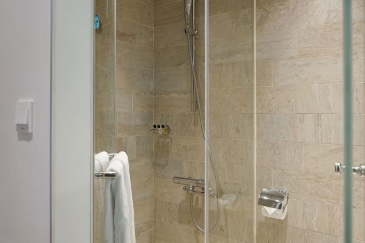 Ducha con cerramiento de vidrio, azulejos color beige, un perchero y un dispensador de jabón.