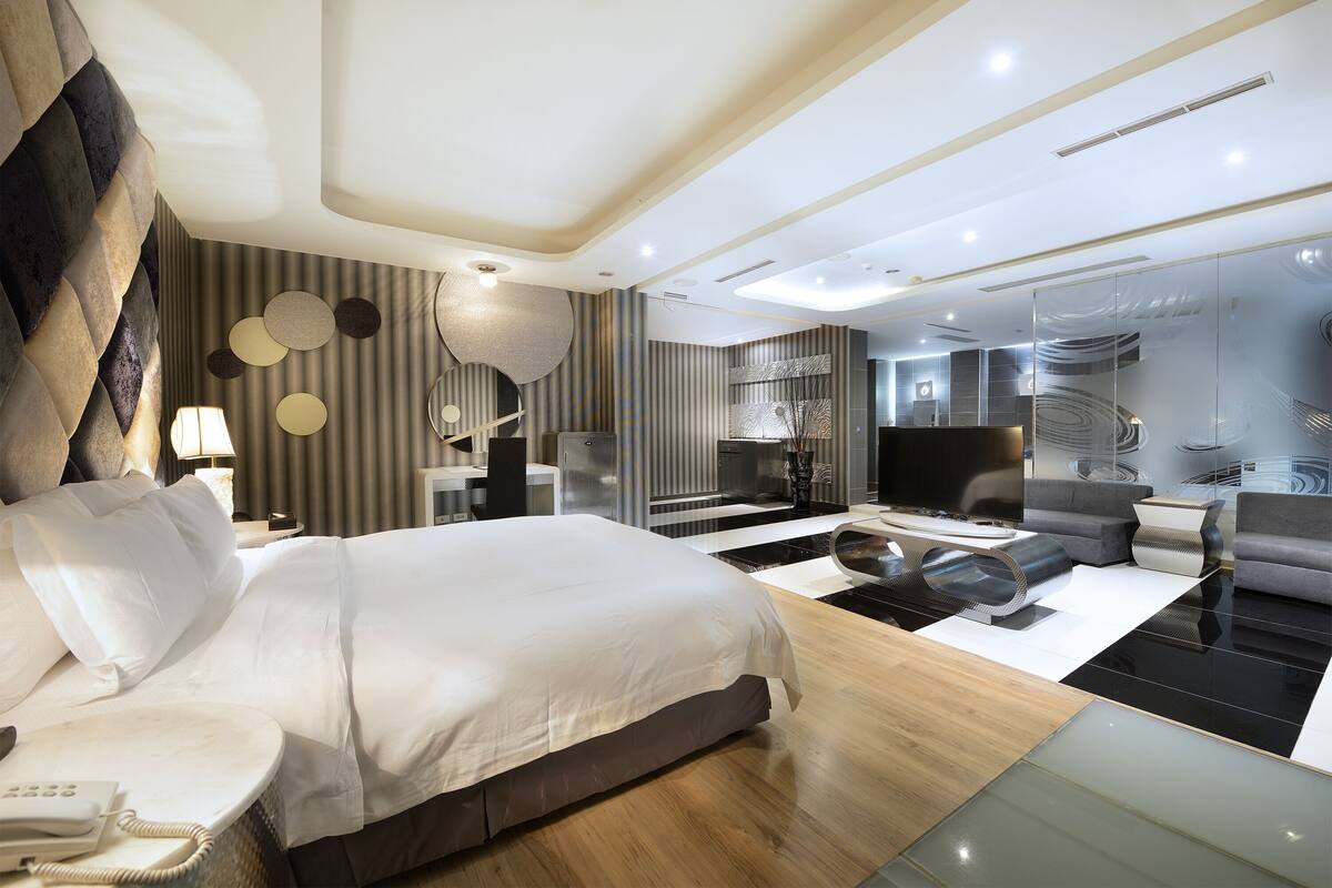 A modern hotel room with a large bed, a desk, a sofa, and a TV.