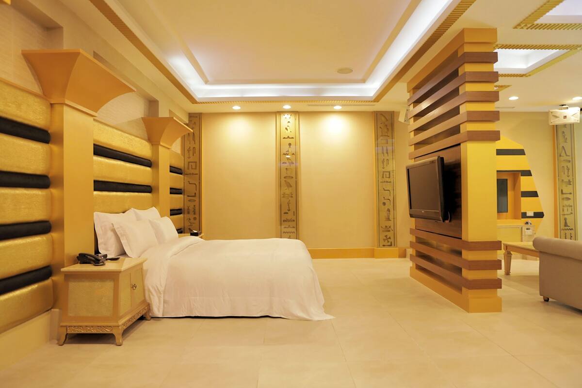 A bedroom with a bed, a nightstand, a TV, and decorative wall panels.