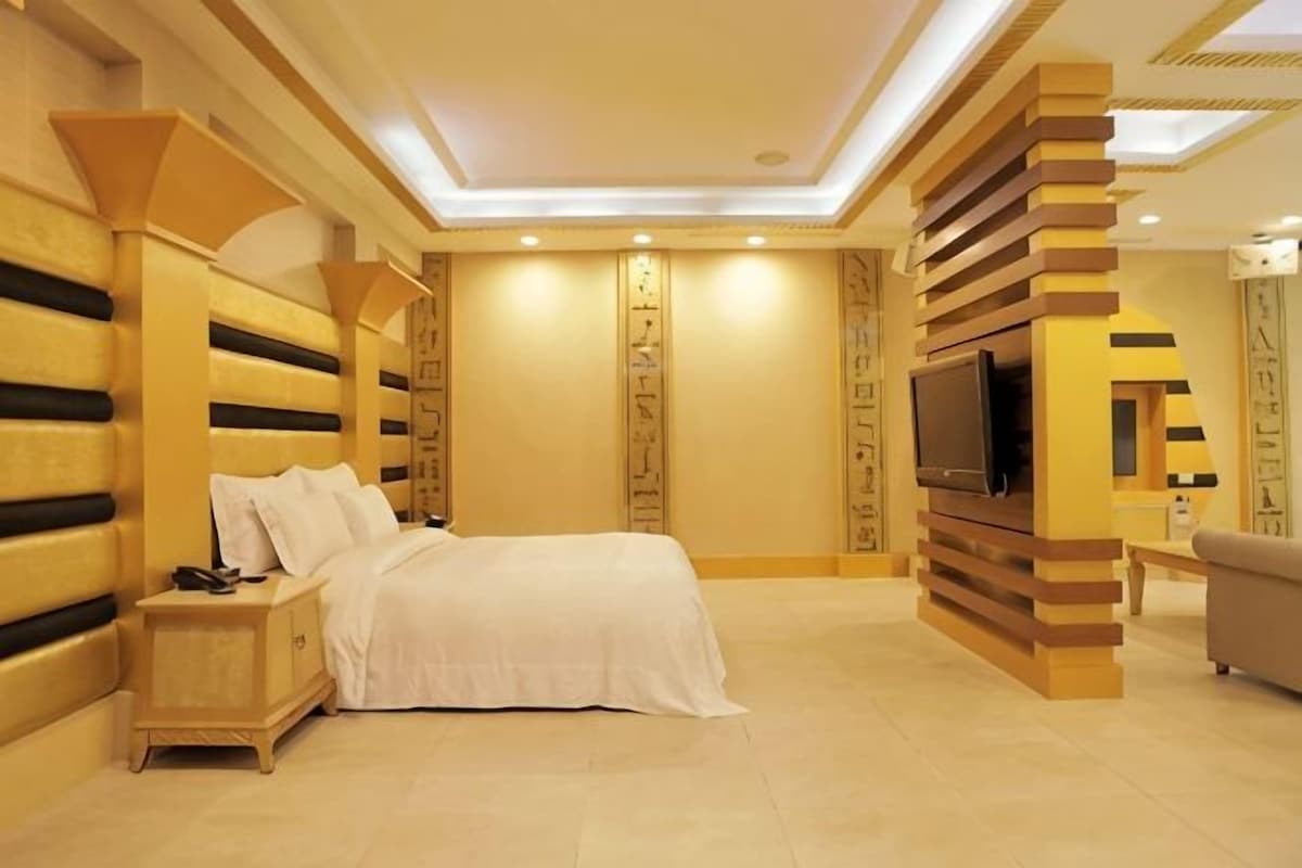 A bedroom with a bed, bedside table, TV, and a sofa.