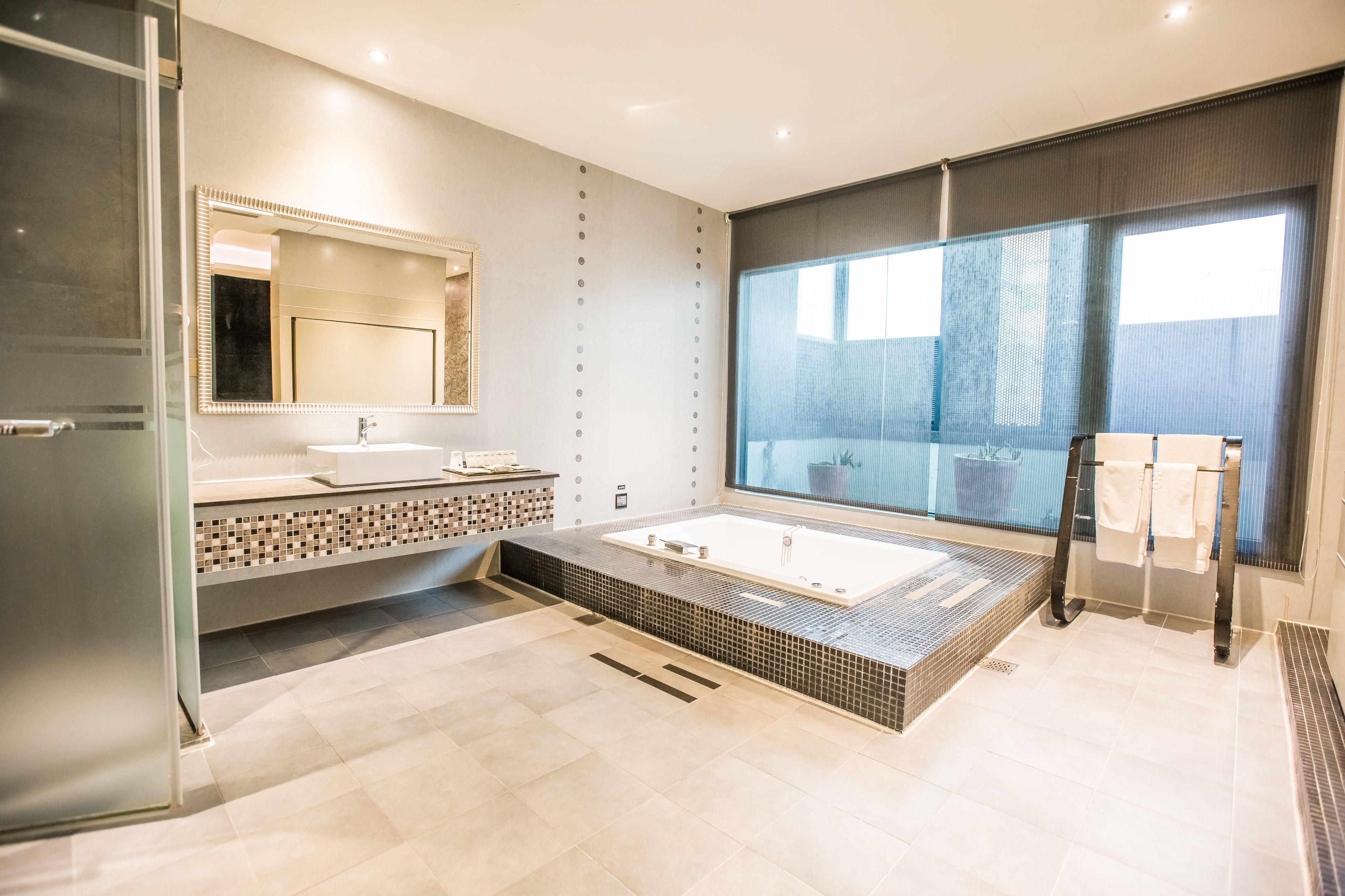 A modern bathroom with a large bathtub, a glass shower enclosure, and a large window providing natural light.