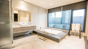 A modern bathroom with a large bathtub, a glass shower enclosure, and a large window providing natural light.