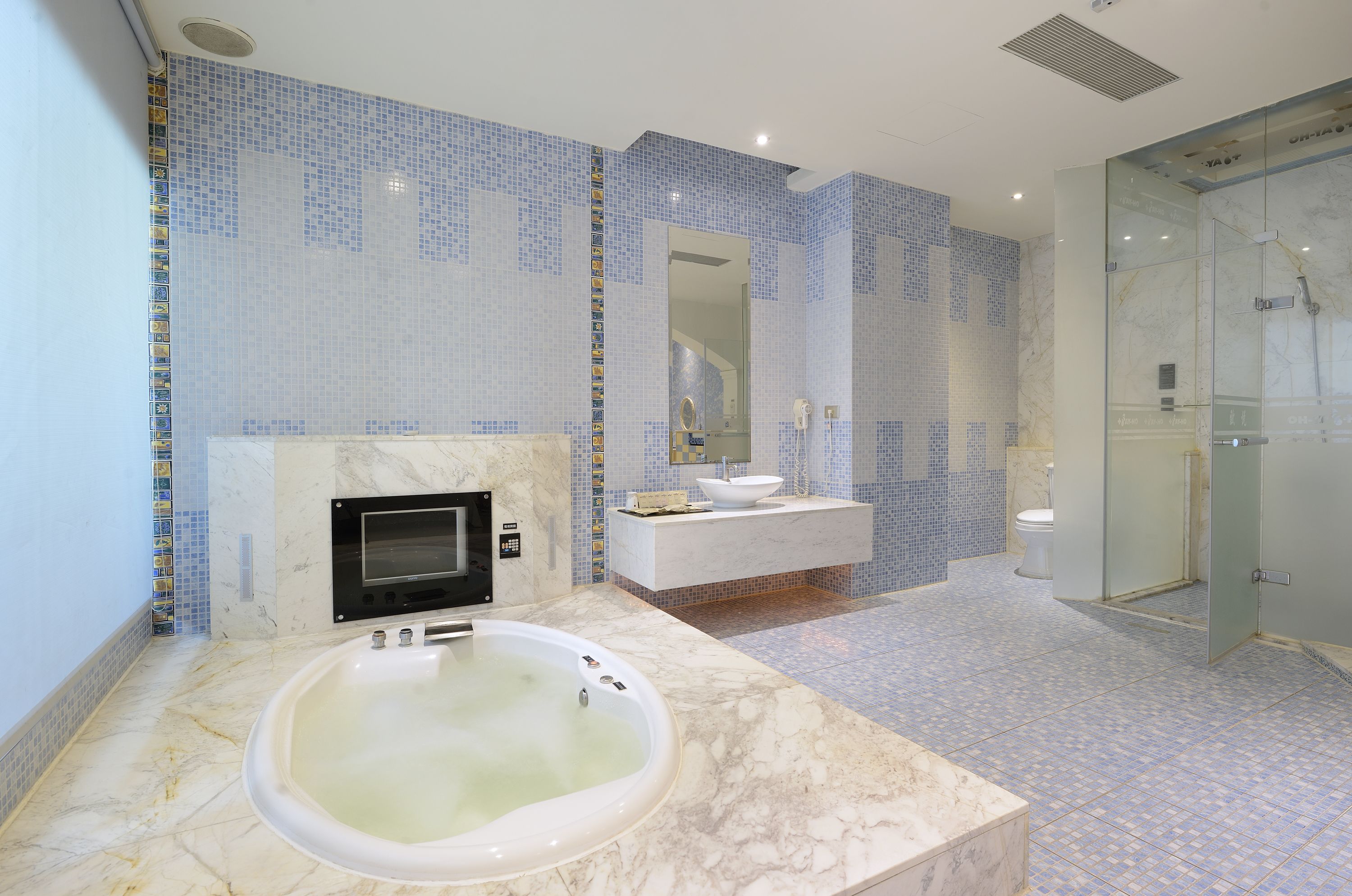 Un baño moderno con una bañera de mármol, ducha con cerramiento de vidrio y tocador blanco con lavamanos y espejo.