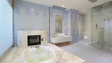 Un baño moderno con una bañera de mármol, ducha con cerramiento de vidrio y tocador blanco con lavamanos y espejo.