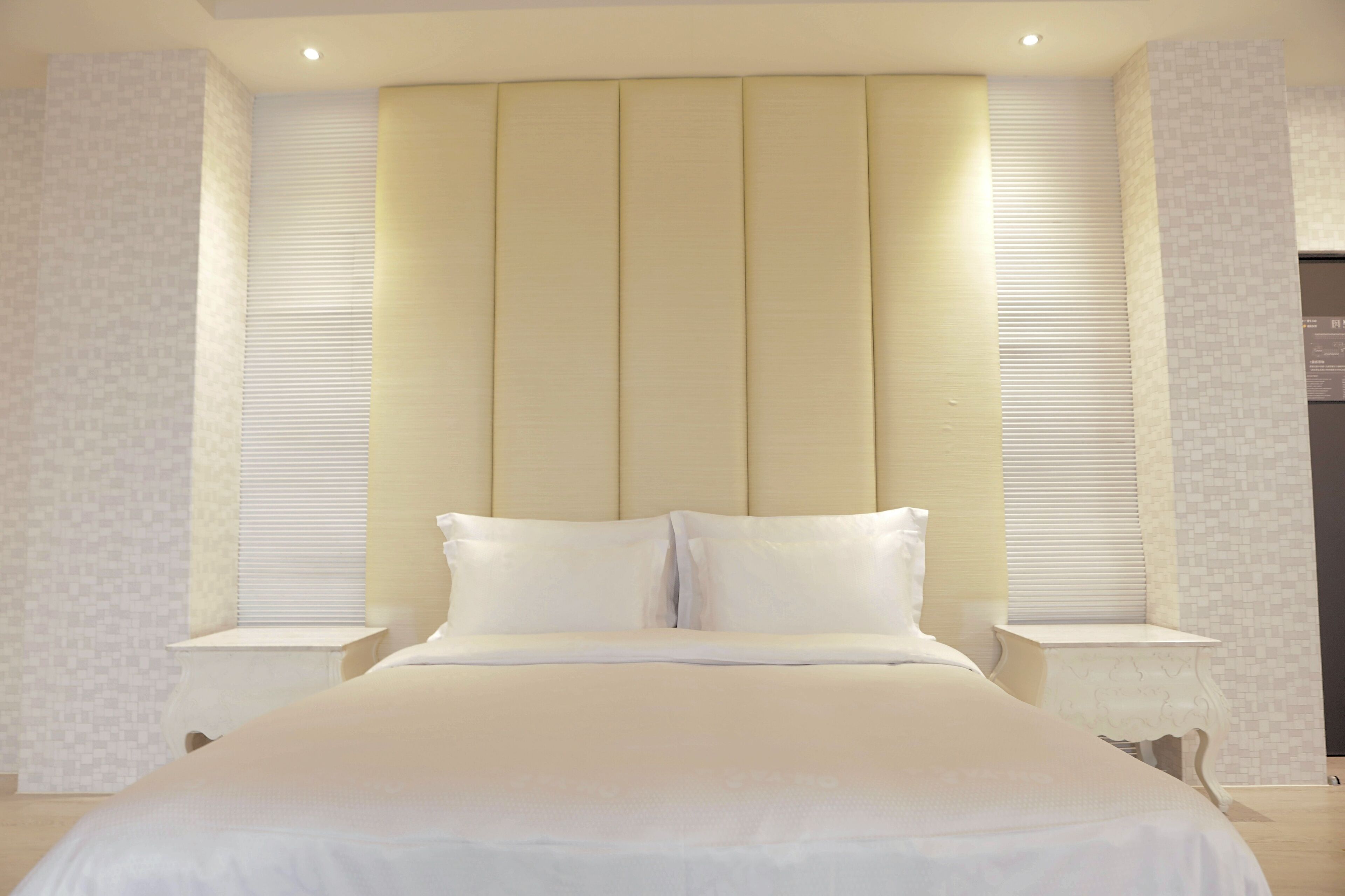 A large bed with a headboard, two bedside tables, and a window with blinds.