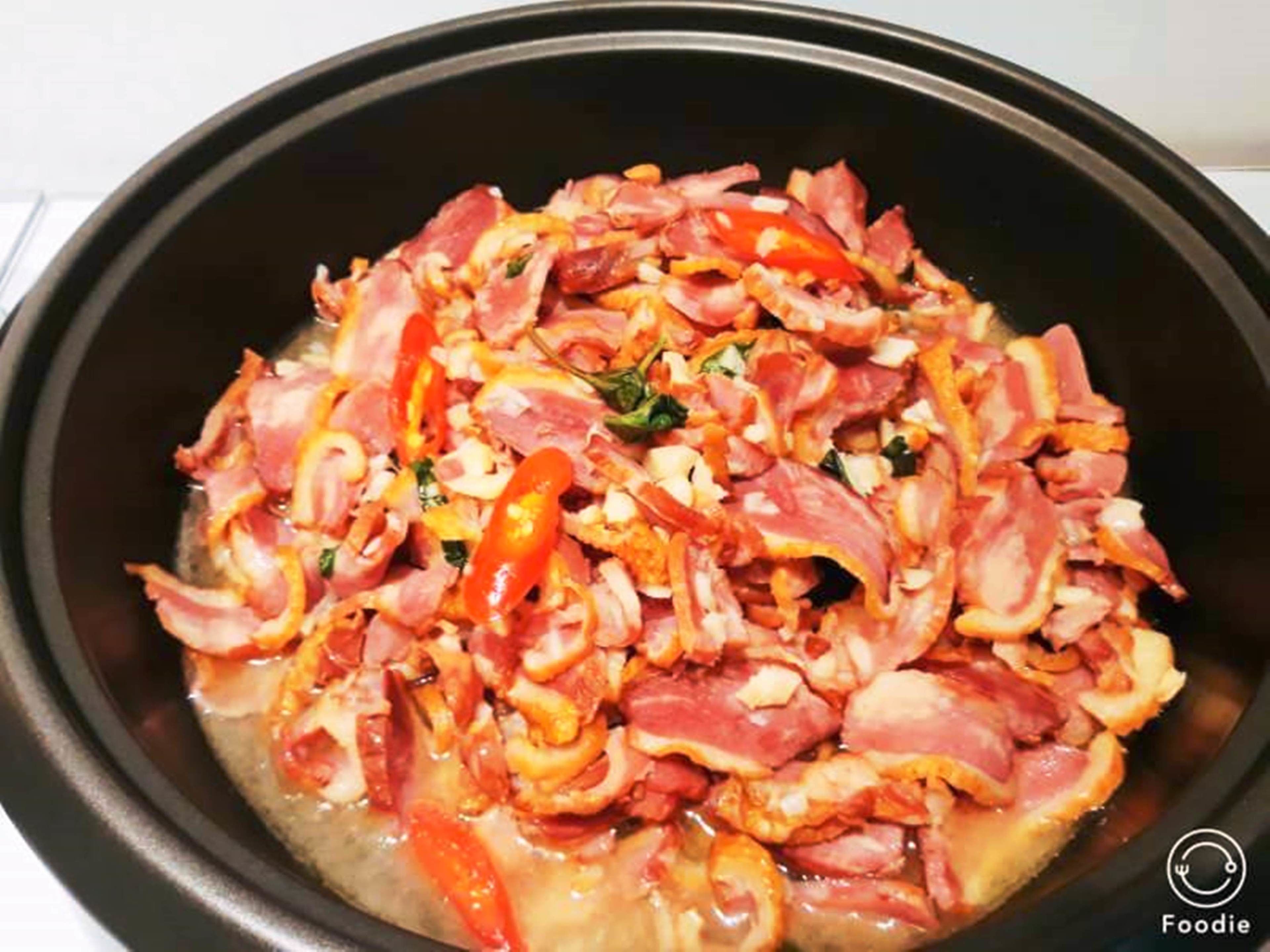 A black pan with cooked bacon, red bell peppers, and onions.