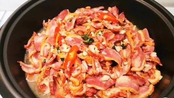 A black pan with cooked bacon, red bell peppers, and onions.