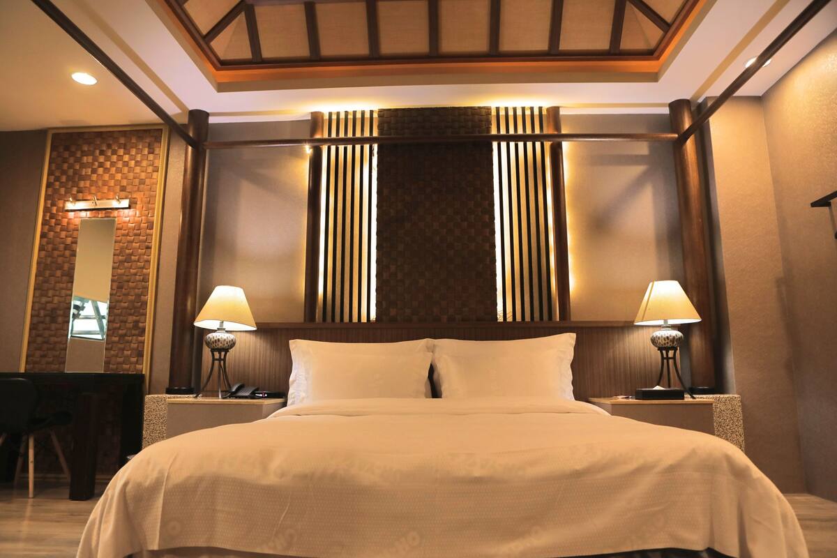 A hotel room with a large bed, two bedside lamps, a desk with a chair, and a mirror on the wall.