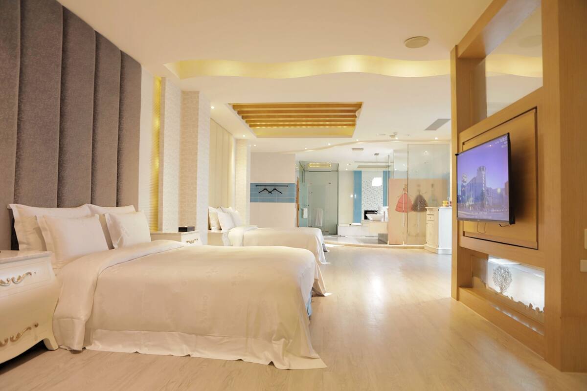 A modern hotel room with a large bed, a TV mounted on the wall, and a separate seating area with a view of the city.