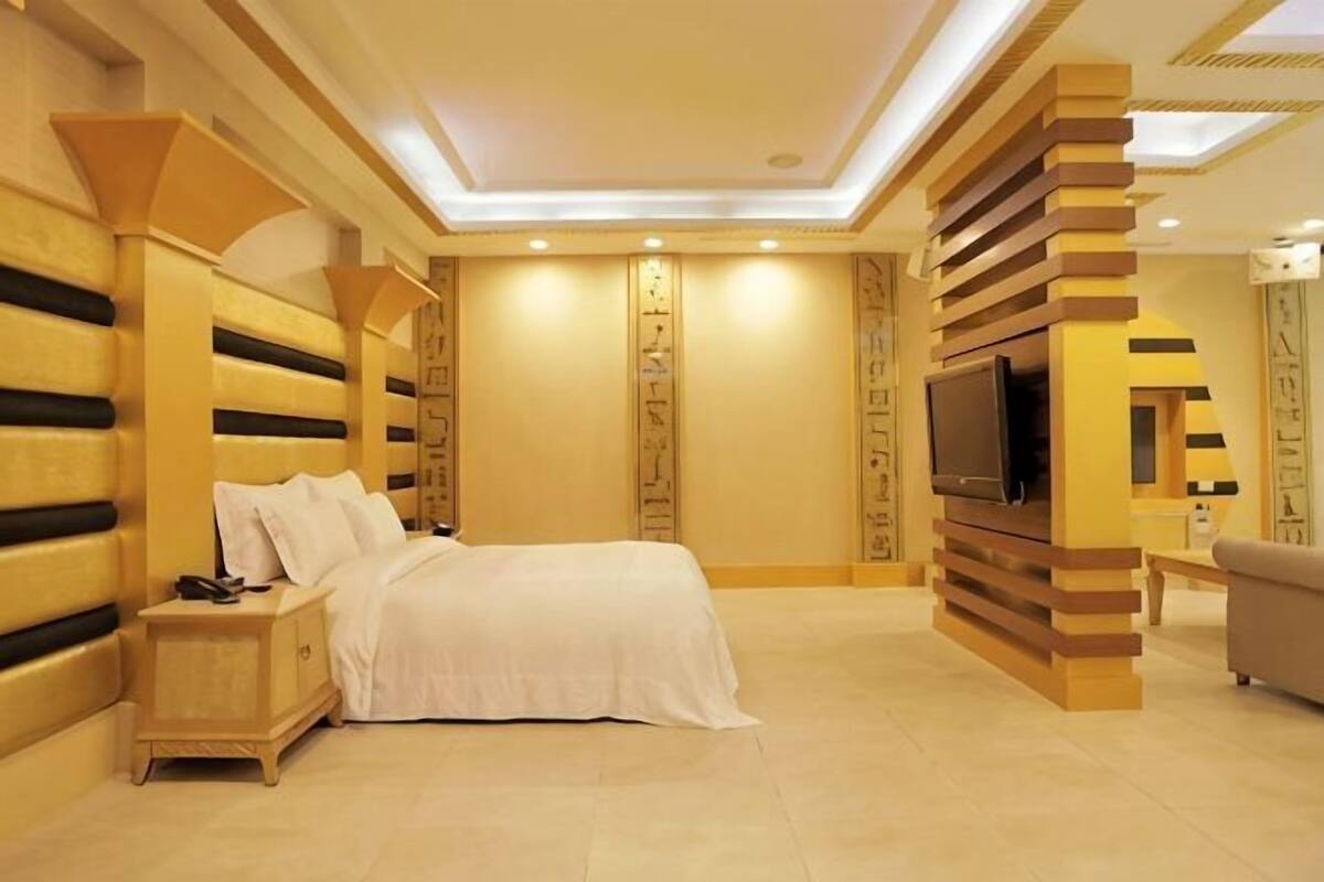 A bedroom with a bed, bedside table, TV, and a sofa.