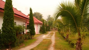 A pathway leading to a building with a red roof, surrounded by greenery and palm trees. - Pingdoi Resort (Mae Sai)