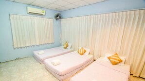 Een hotelkamer met drie bedden, witte gordijnen, een airconditioningsunit en een ventilator.