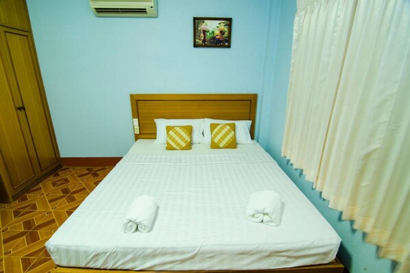 Una cama bien hecha con sábanas blancas y dos toallas, un cabecero de madera, un aire acondicionado de pared y un cuadro sobre la cama.