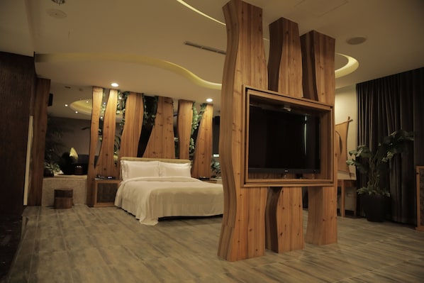 A modern bedroom with a large TV mounted on a wooden structure, a bed with white bedding, and a small bedside table.
