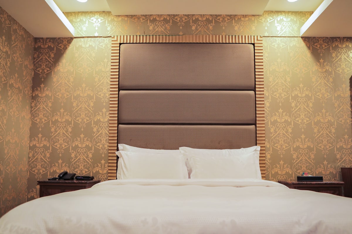 A hotel room with a large bed, a headboard, and a nightstand with a telephone.