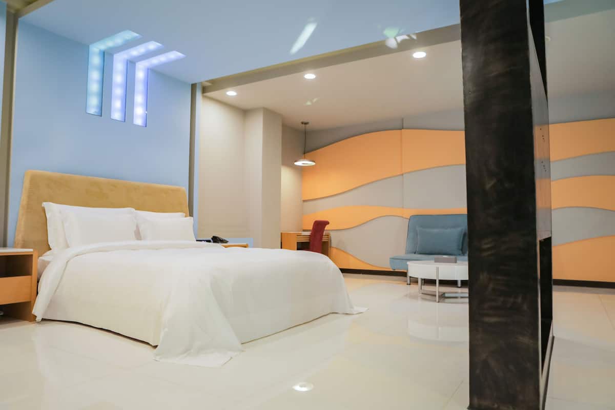 A modern hotel room with a large bed, a desk, a chair, and a curved wall with lighting.