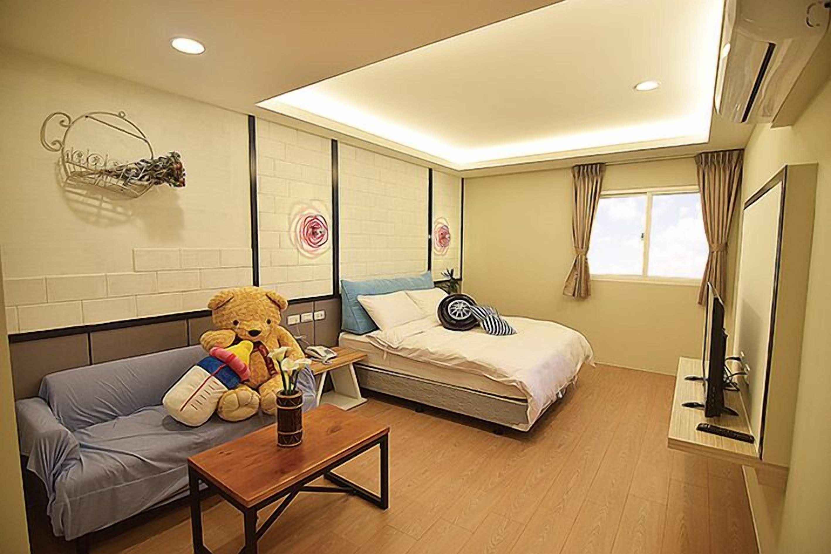 A hotel room with a sofa, a bed, a wooden table, and a teddy bear.