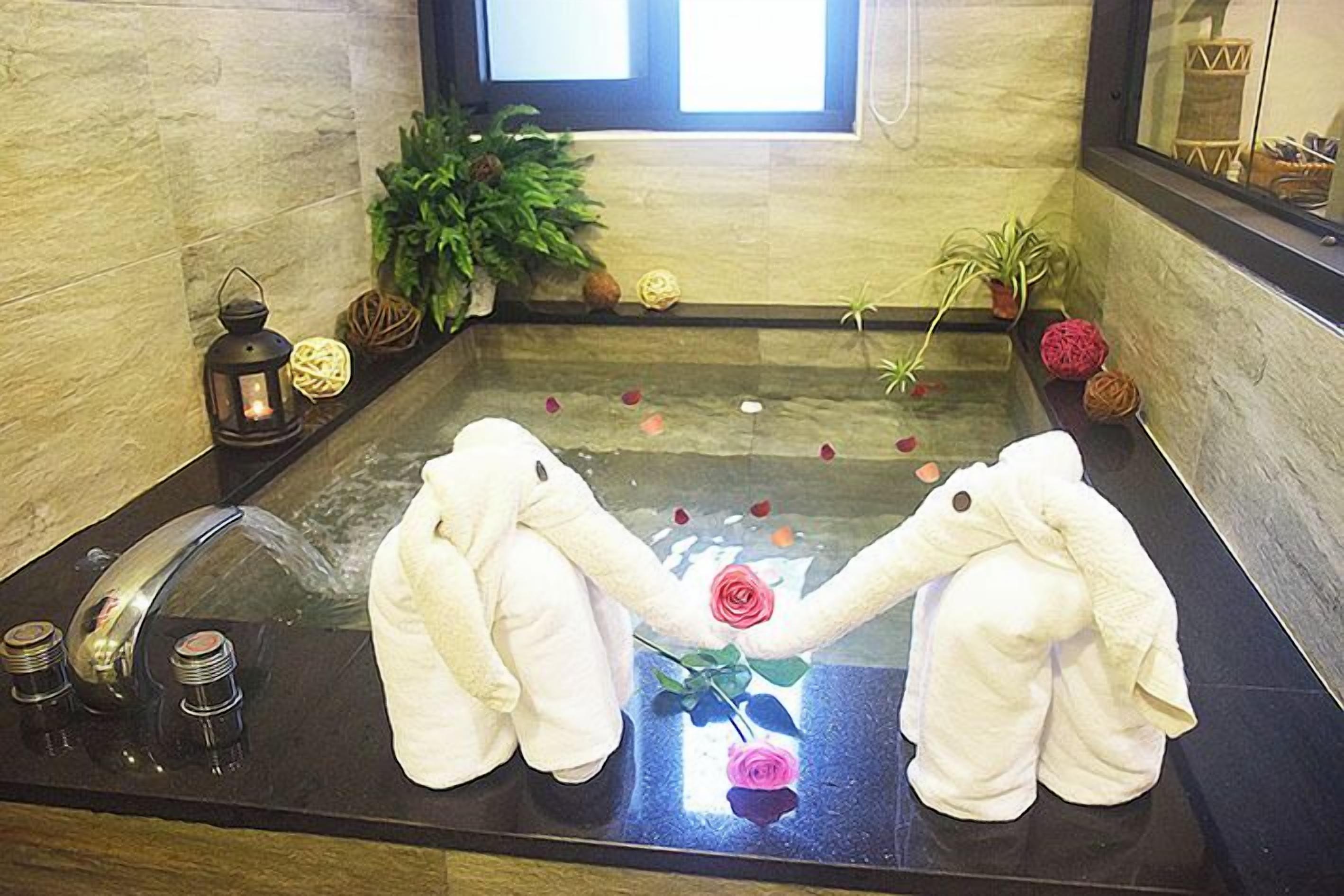 Eine Badewanne mit zwei weißen Elefantenhandtüchern, einer Rose und Dekorationsgegenständen.