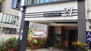 Ein modernes Gebäude mit der Nummer 21, mit dem Schild "Hot Spring BnB". Es hat eine glatte Fassade, viele Fenster und Blumentöpfe am Eingang.